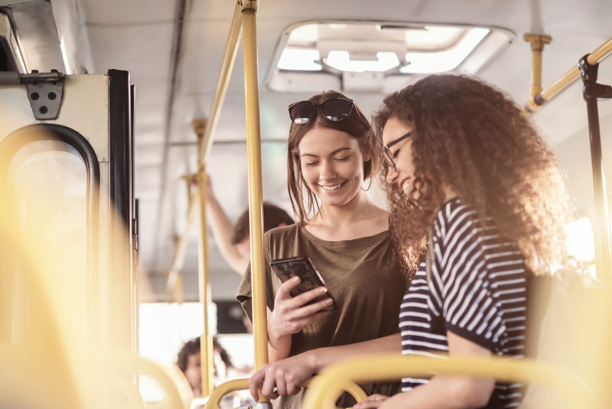 Two woman riding a bus looking at a cell phone