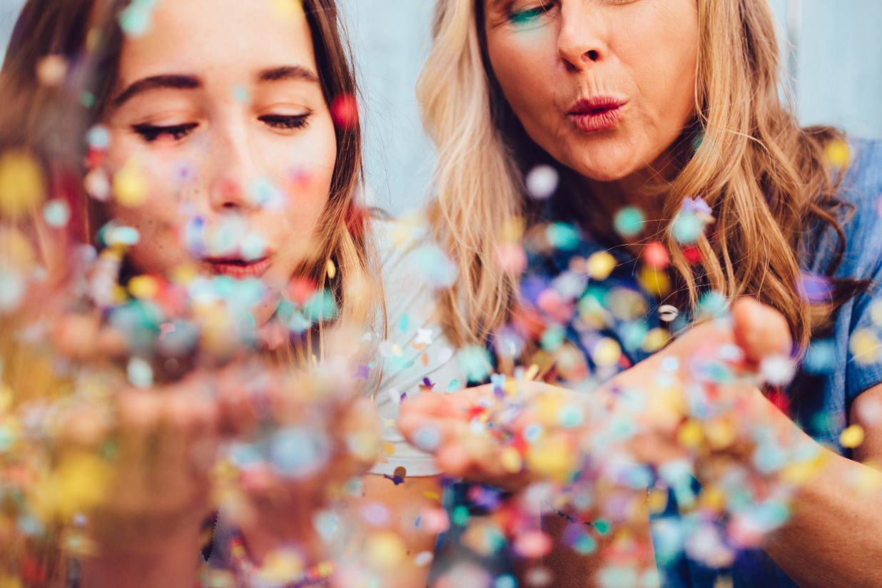 Two women blowing confetti into the camera