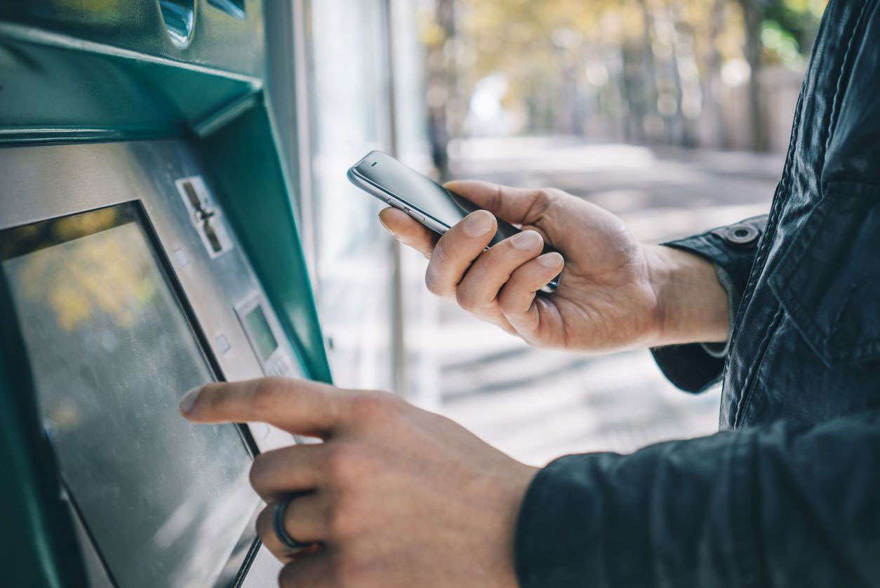 Man using ATM machine with smartphone in hand