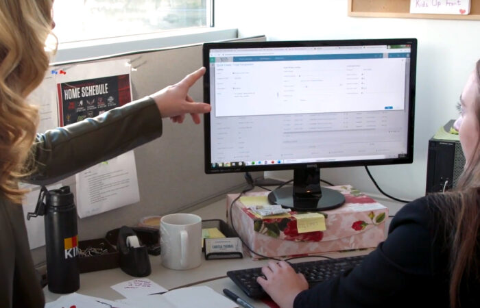 Two people working together in front of a computer monitor