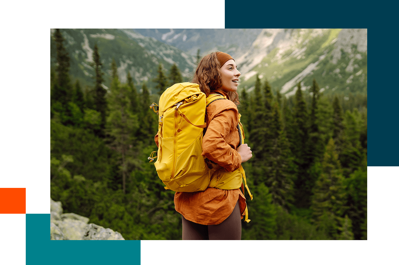 Woman with orange jacket and yellow backpack walking through a forest