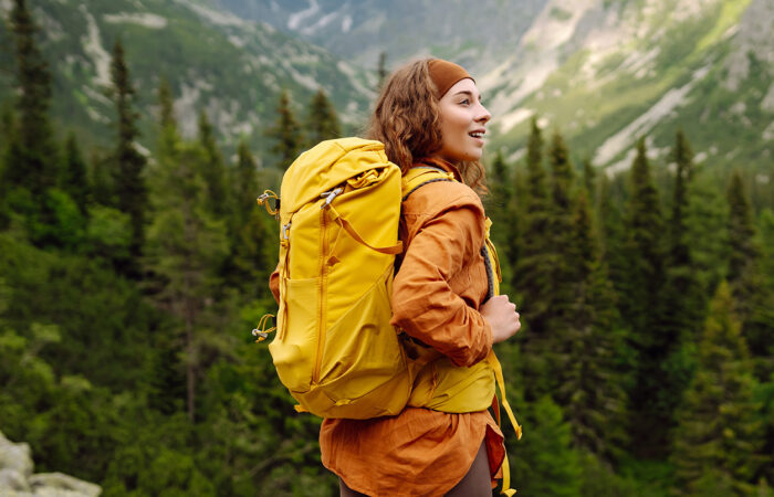 Woman with orange jacket and yellow backpack walking through a forest
