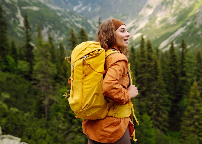 Woman with orange jacket and yellow backpack walking through a forest