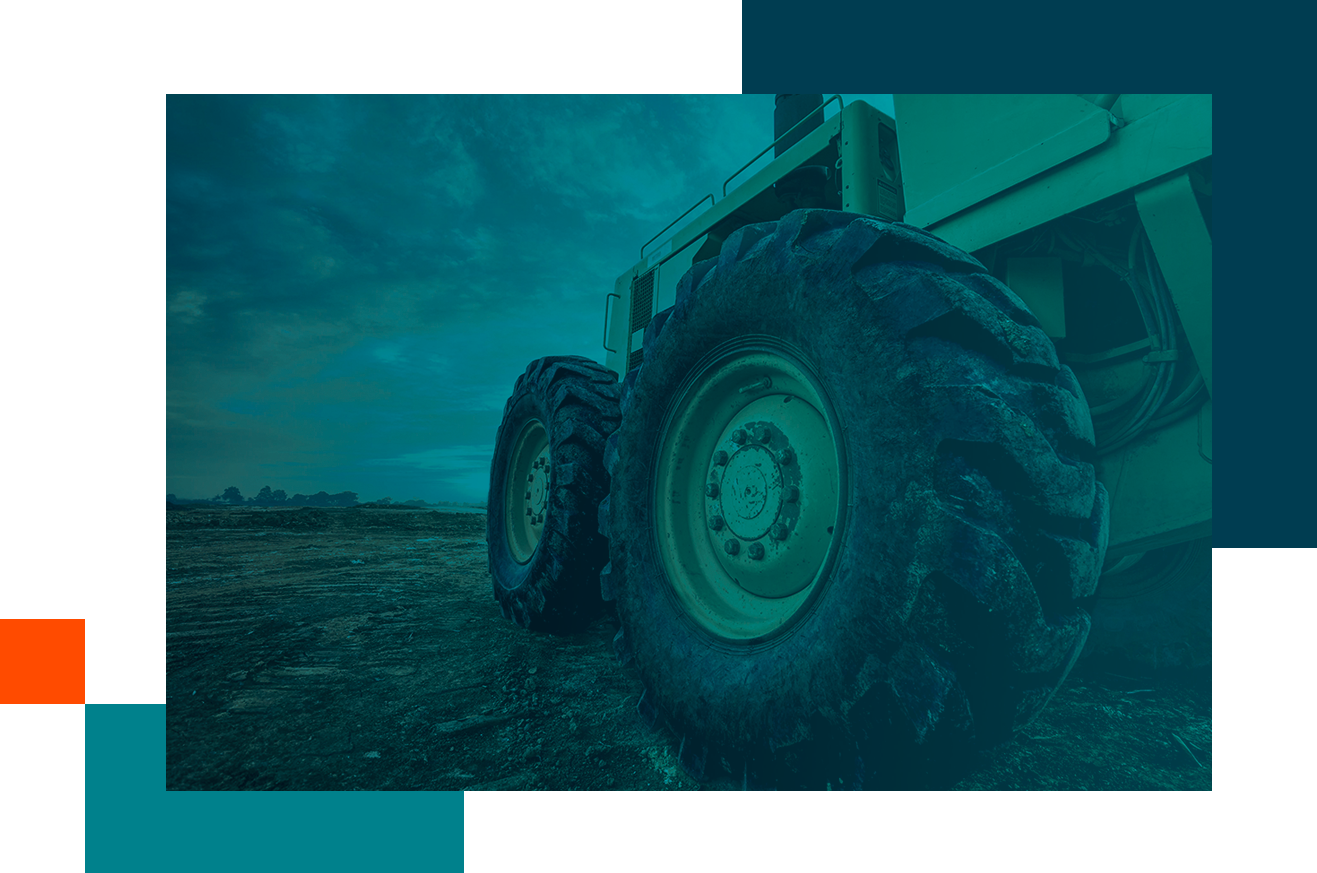 A close-up of large tires on heavy-duty equipment, positioned on rough terrain under a cloudy sky.