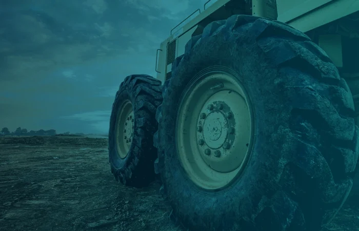 A close-up of large tires on heavy-duty equipment, positioned on rough terrain under a cloudy sky.