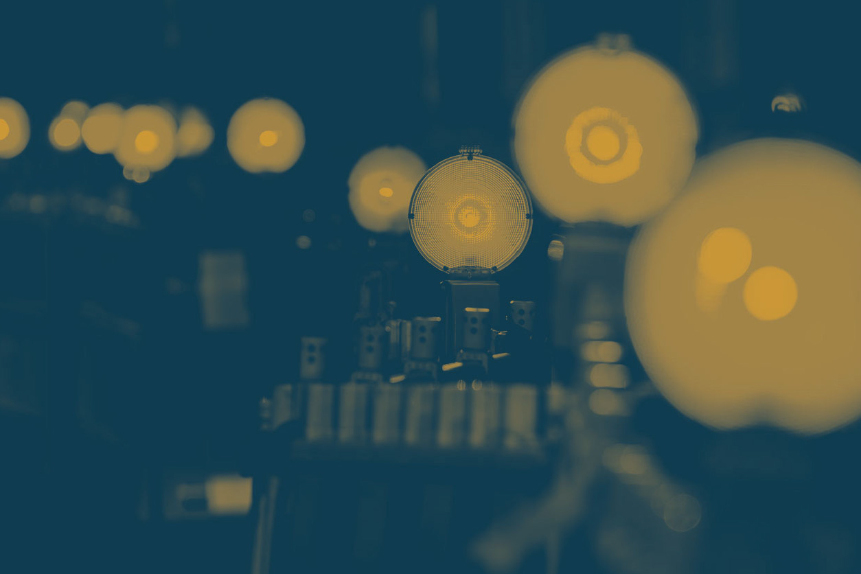 Row of illuminated light bulbs with a central bulb in sharp focus against a dark background, highlighting filament details and industrial setup.