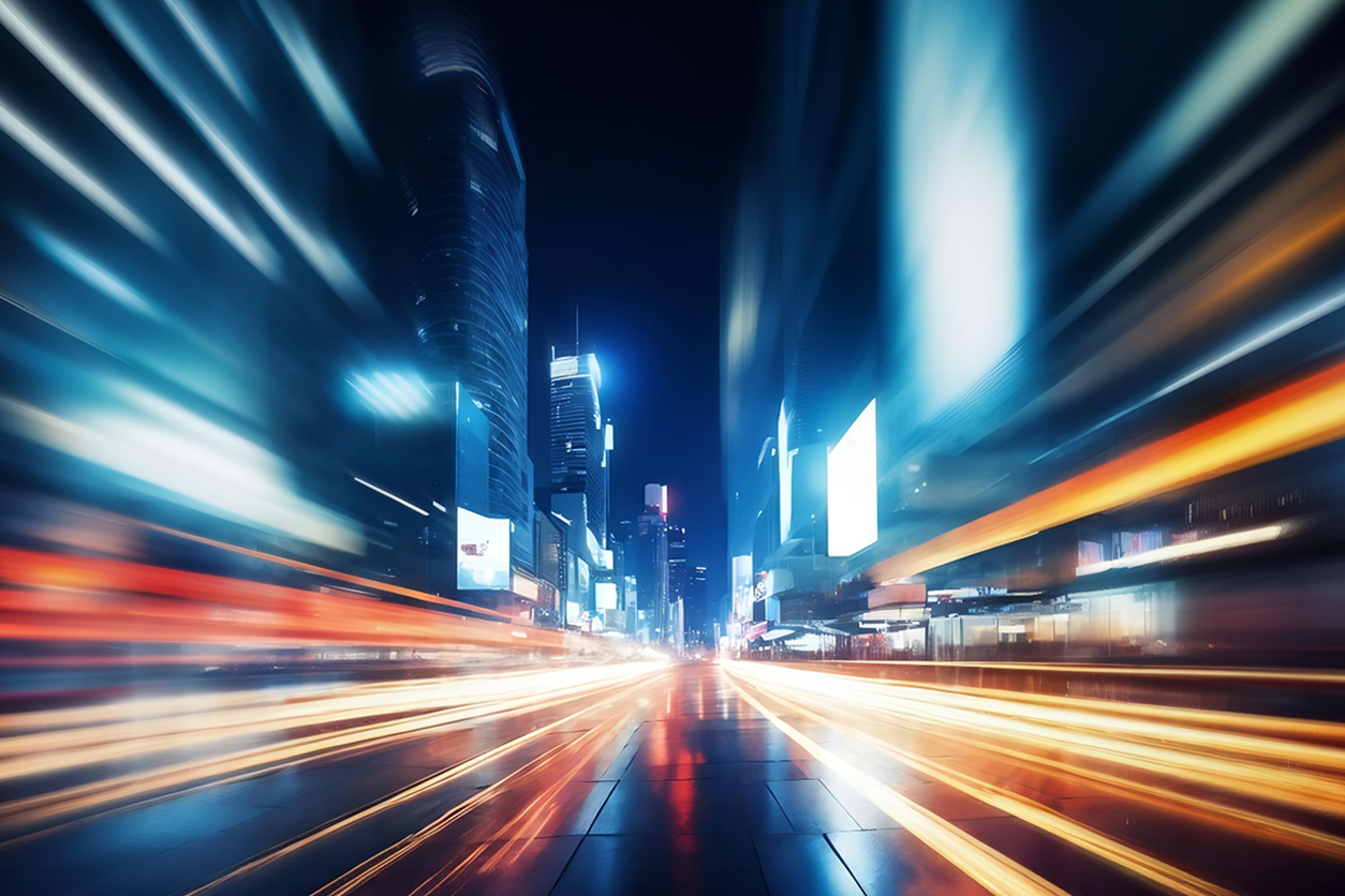 Dynamic cityscape at night with bright light trails from fast-moving traffic, surrounded by illuminated skyscrapers and glowing billboards.