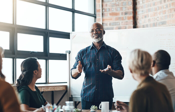 Person presenting to a group in a bright office meeting room with a whiteboard in the background