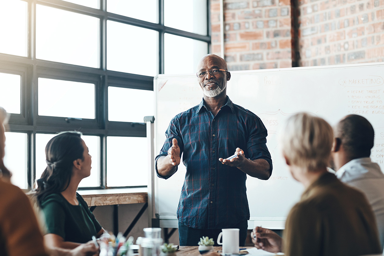 Person presenting to a group in a bright office meeting room with a whiteboard in the background