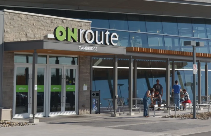 ONroute Cambridge service centre exterior with glass façade, entrance doors and people seated outside.