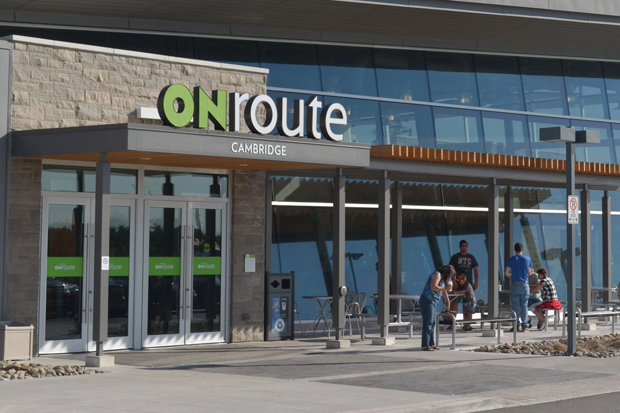 ONroute Cambridge service centre exterior with glass façade, entrance doors and people seated outside.
